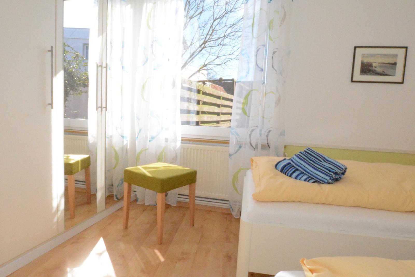 Schlafzimmer mit Bett, Stuhl und Fenster mit Vorhängen.