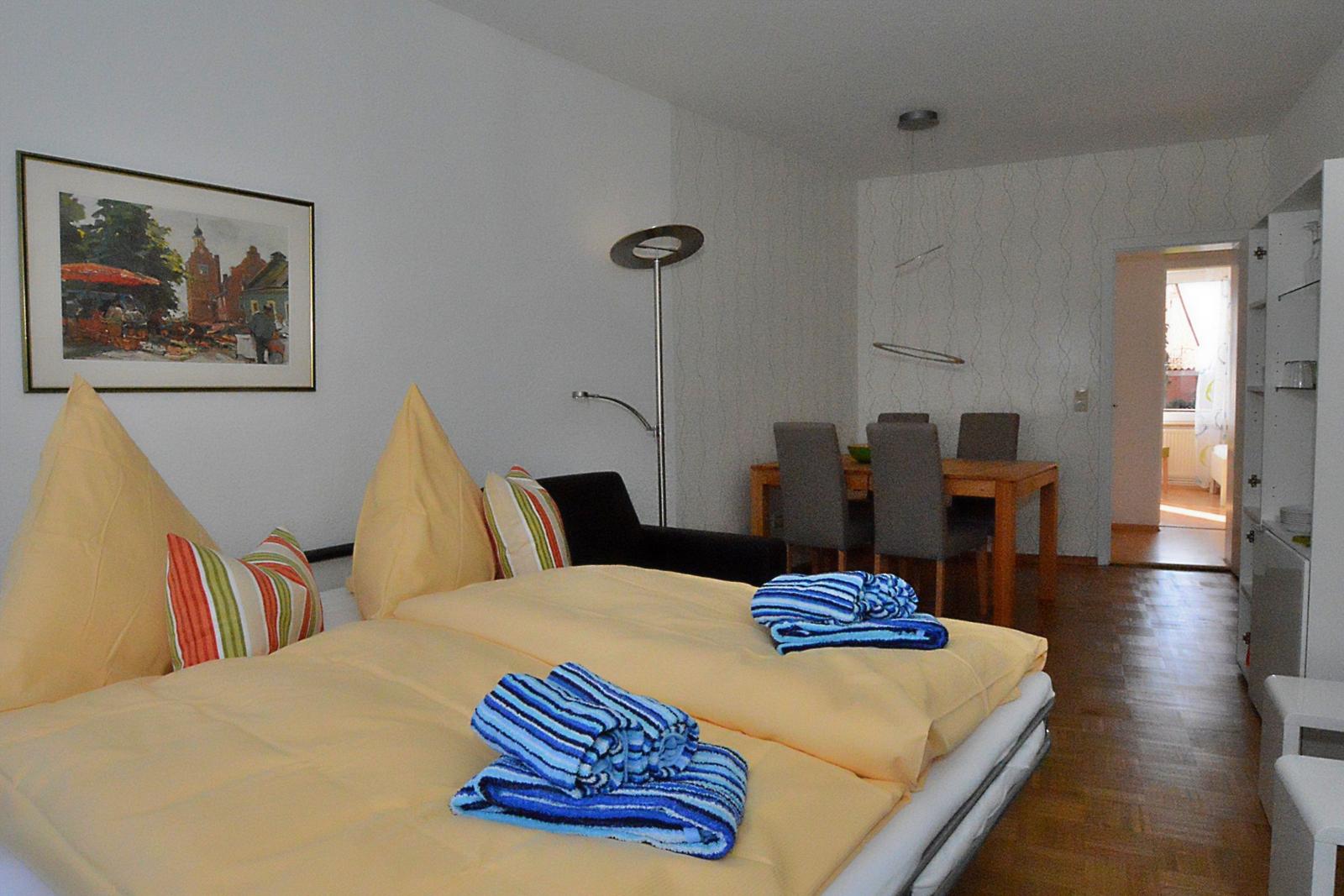 Schlafzimmer mit Bett, Wandbild und angrenzender Essnische mit Tisch und Stühlen.