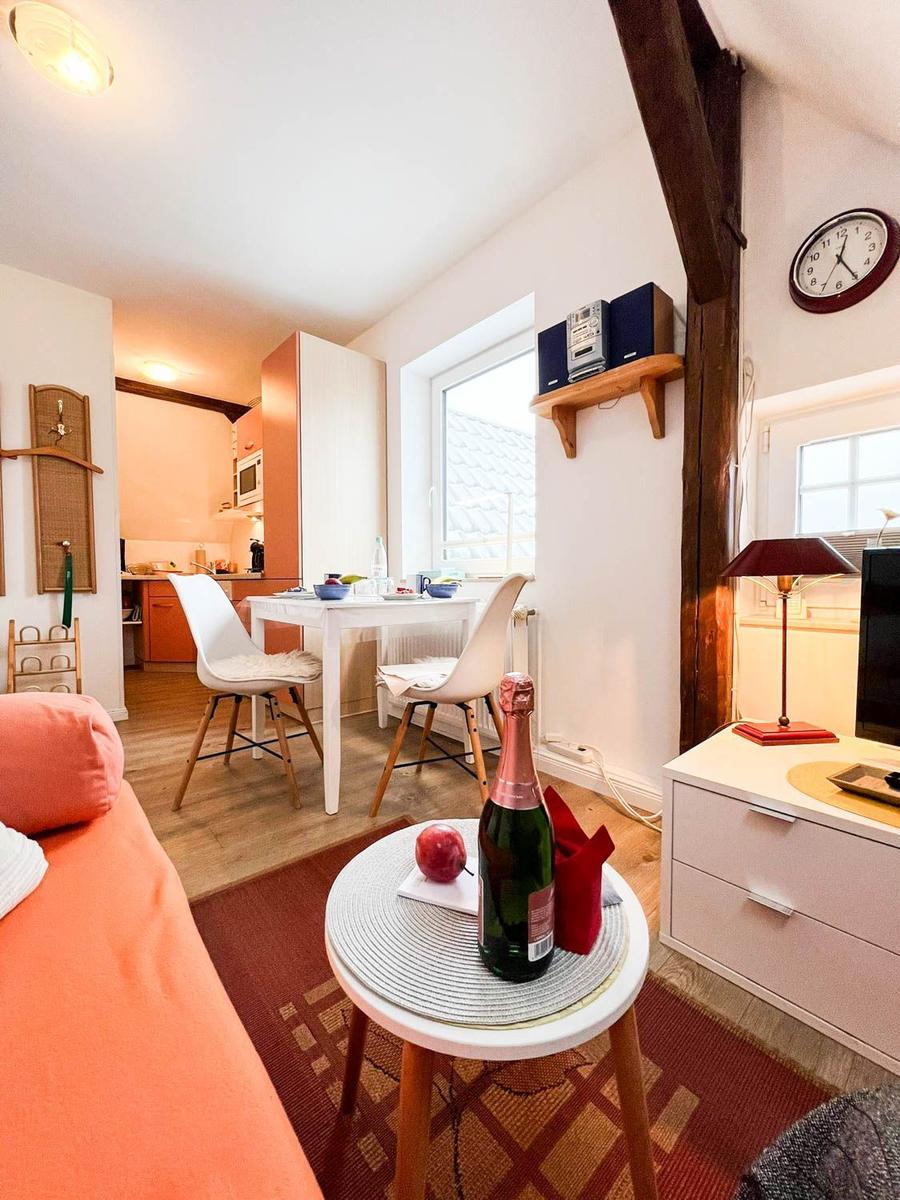 Wohnbereich mit Esstisch, Sofa und Fernseher. Holzbalken und Küchenbereich sichtbar.