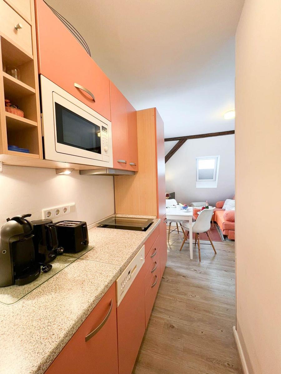 Küche mit Mikrowelle und Arbeitsfläche, Blick in Wohnbereich mit Tisch und Sofa.