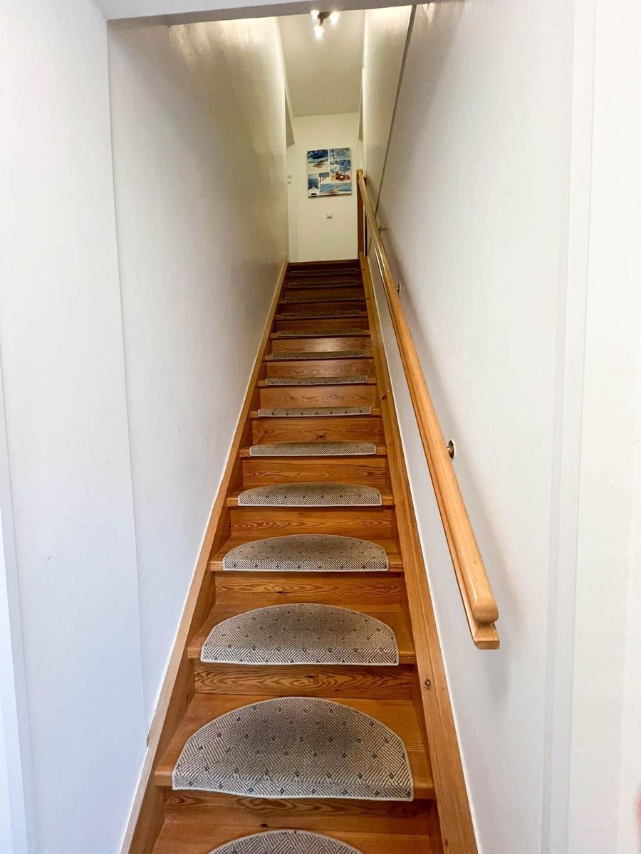Holztreppe mit Teppichstufen und Geländer führt nach oben.
