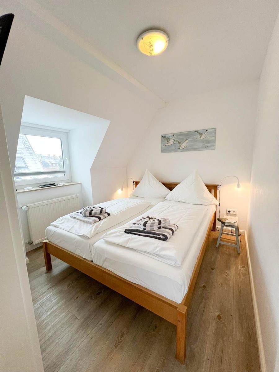 Schlafzimmer mit Doppelbett, Holzboden und Fenster. Wandbild mit Vögeln.