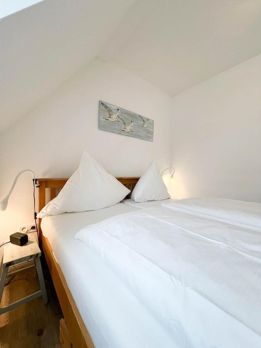 Schlafzimmer mit Doppelbett, Holzrahmen, weißen Bettwäsche und Wandbild mit Vögeln.