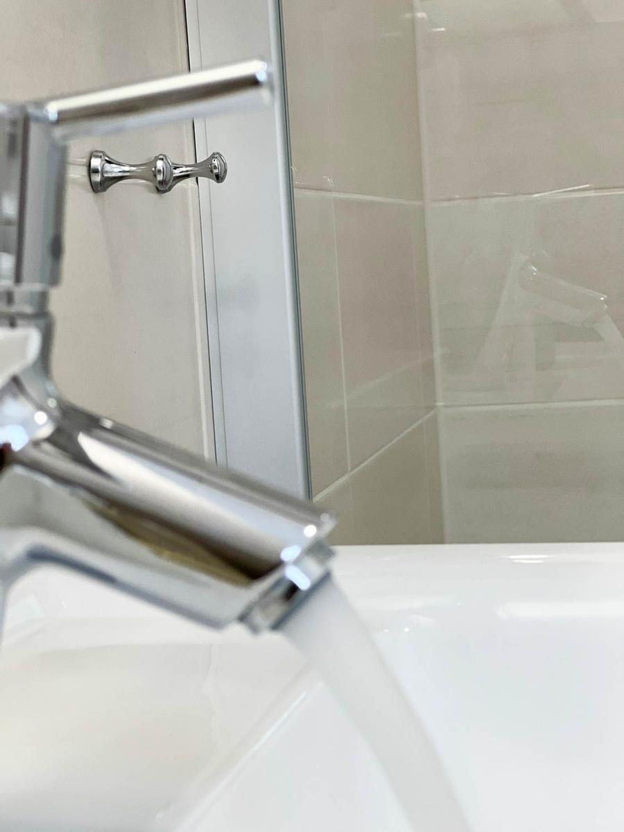 Duschkabine mit Glaswand und Chromarmatur. Wasser fließt in die Badewanne.