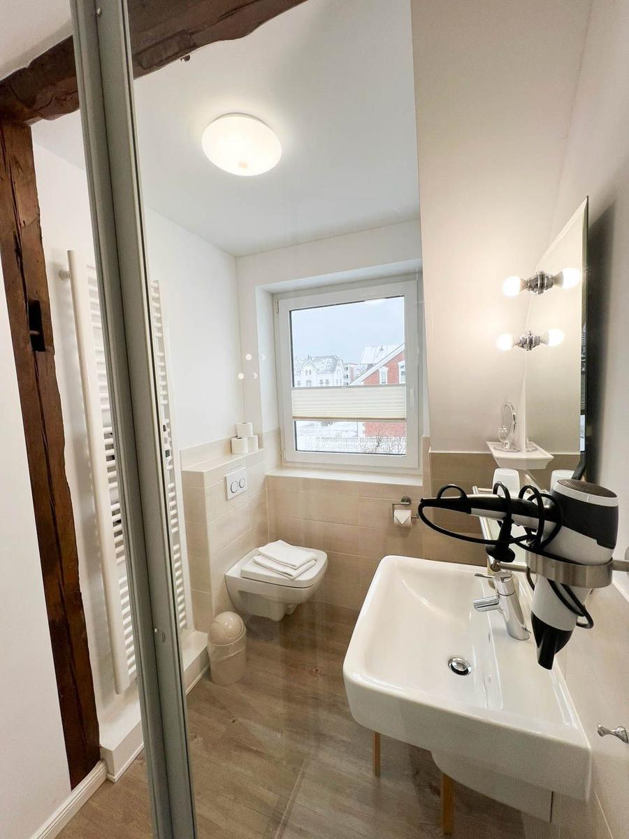 Badezimmer mit Toilette, Waschbecken und Fenster. Haartrockner und Spiegel vorhanden.
