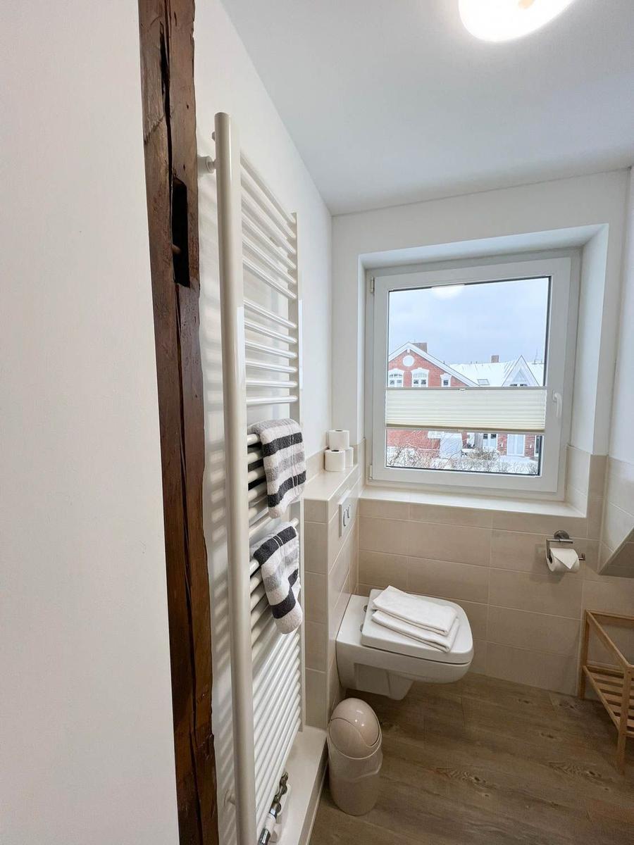 Badezimmer mit Toilette, Heizkörper und Fenster mit Blick auf Gebäude.