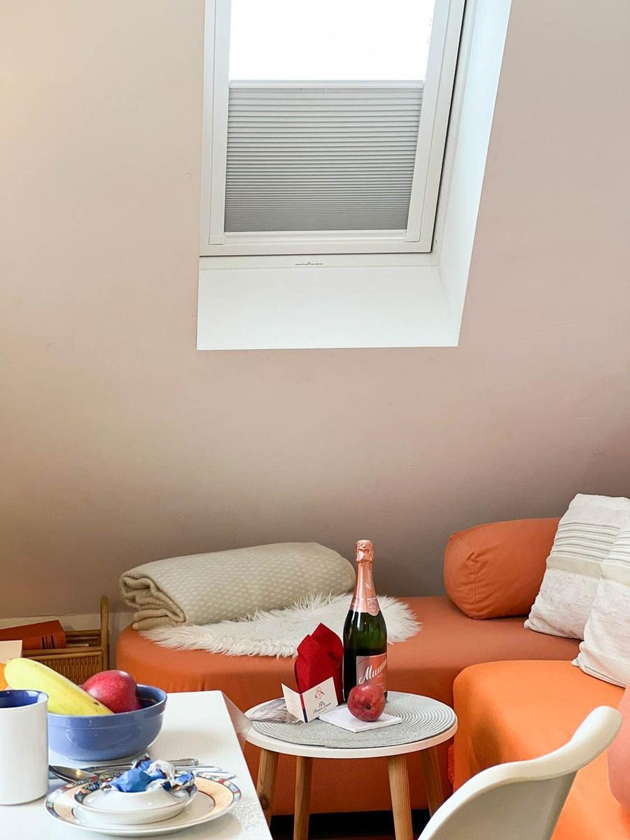 Orange Sofa mit Kissen, Tisch mit Flasche und Obst, Fenster mit Jalousie