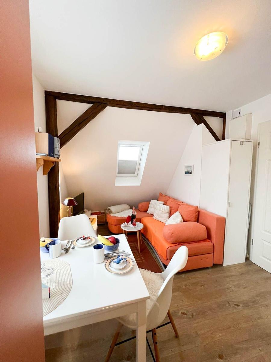 Wohn- und Essbereich mit orangefarbenem Sofa, weißem Tisch und Holzboden.