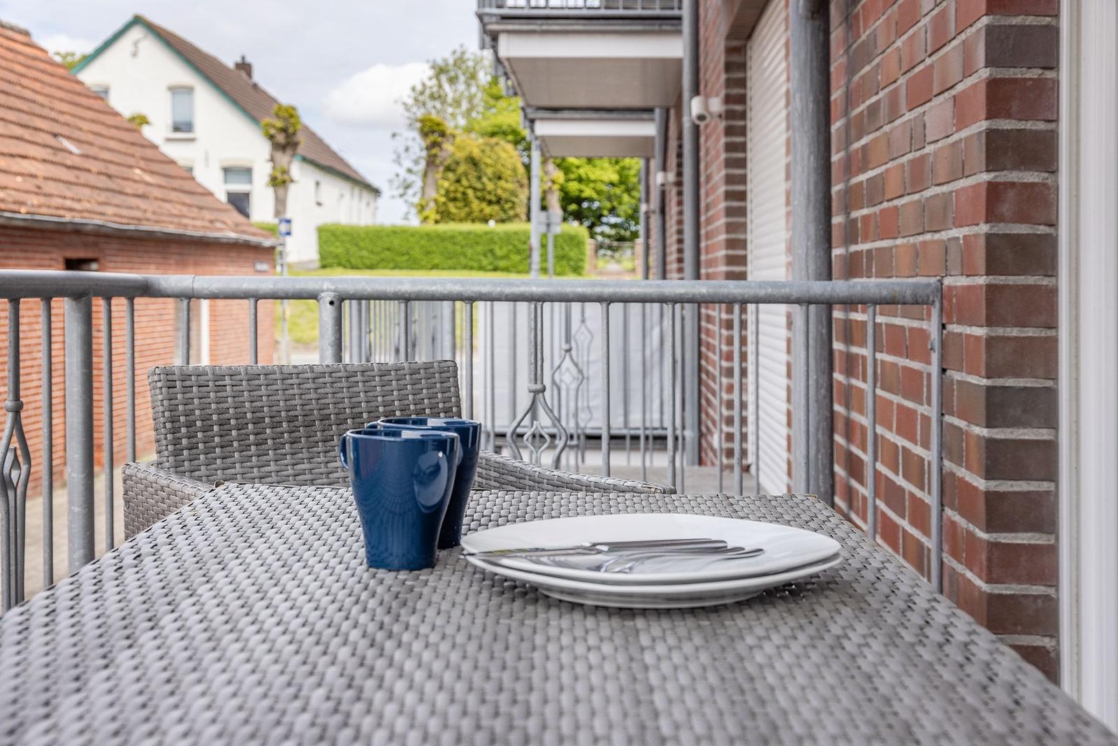 Terrasse mit Tisch, Stühlen und Geschirr. Blick auf Haus und Grünflächen.