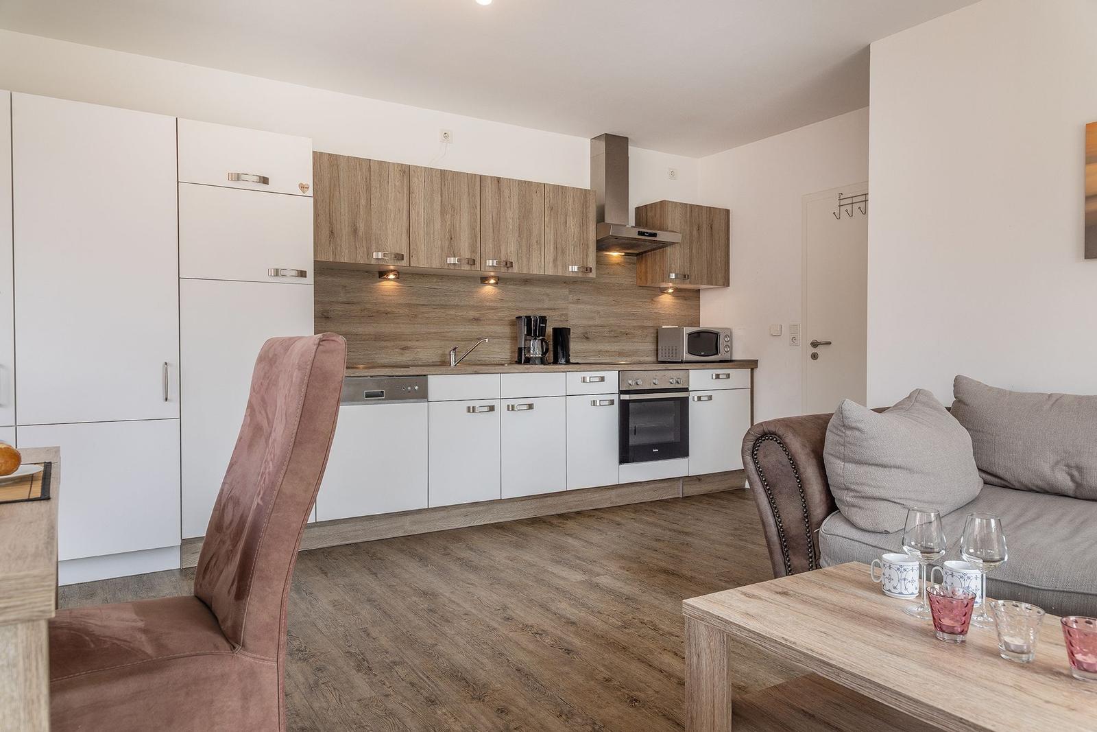 Küche mit Holzoptik und Wohnbereich mit Sofa und Couchtisch.