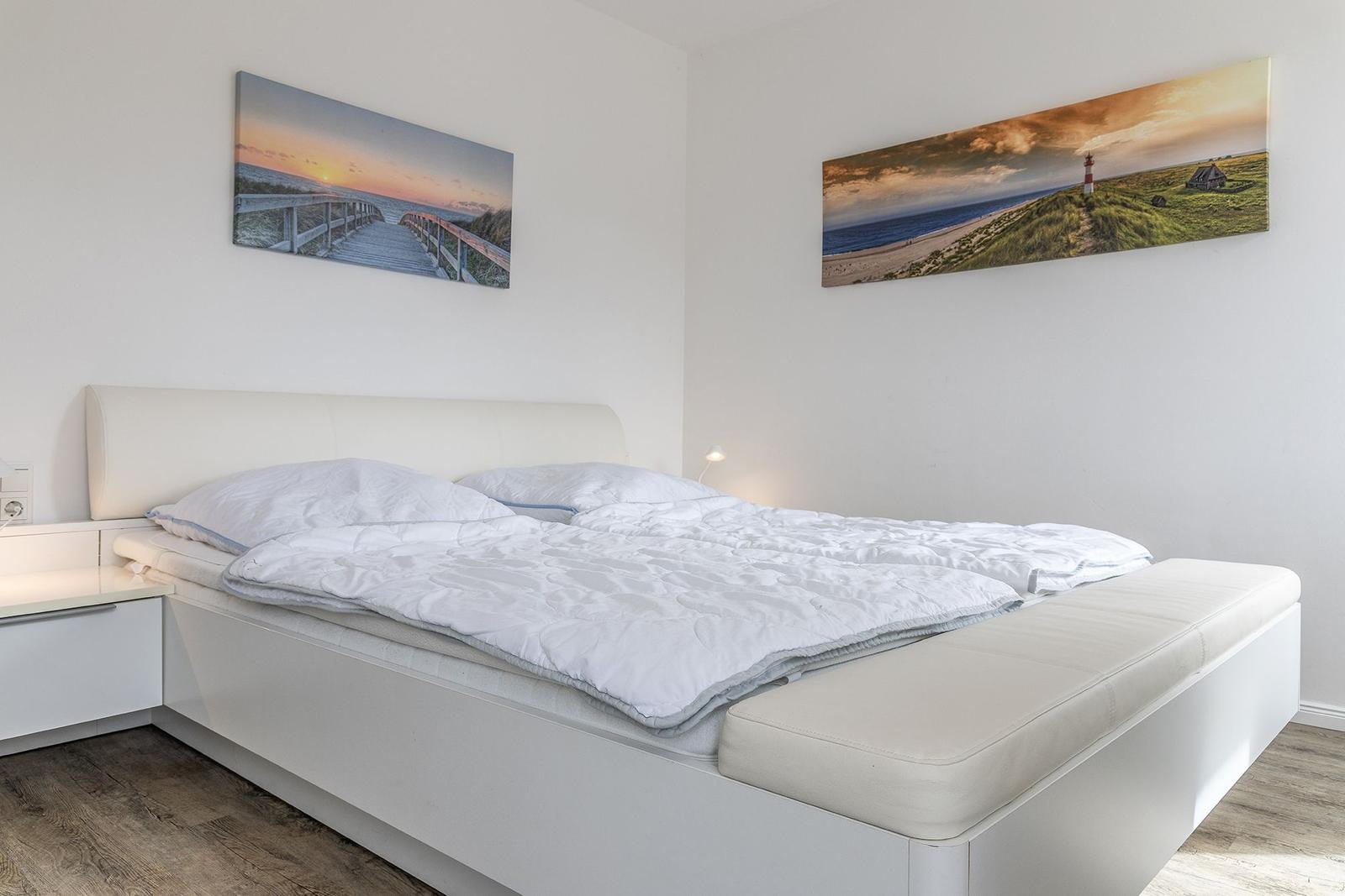 Schlafzimmer mit weißem Bett und Strandbildern an den Wänden.