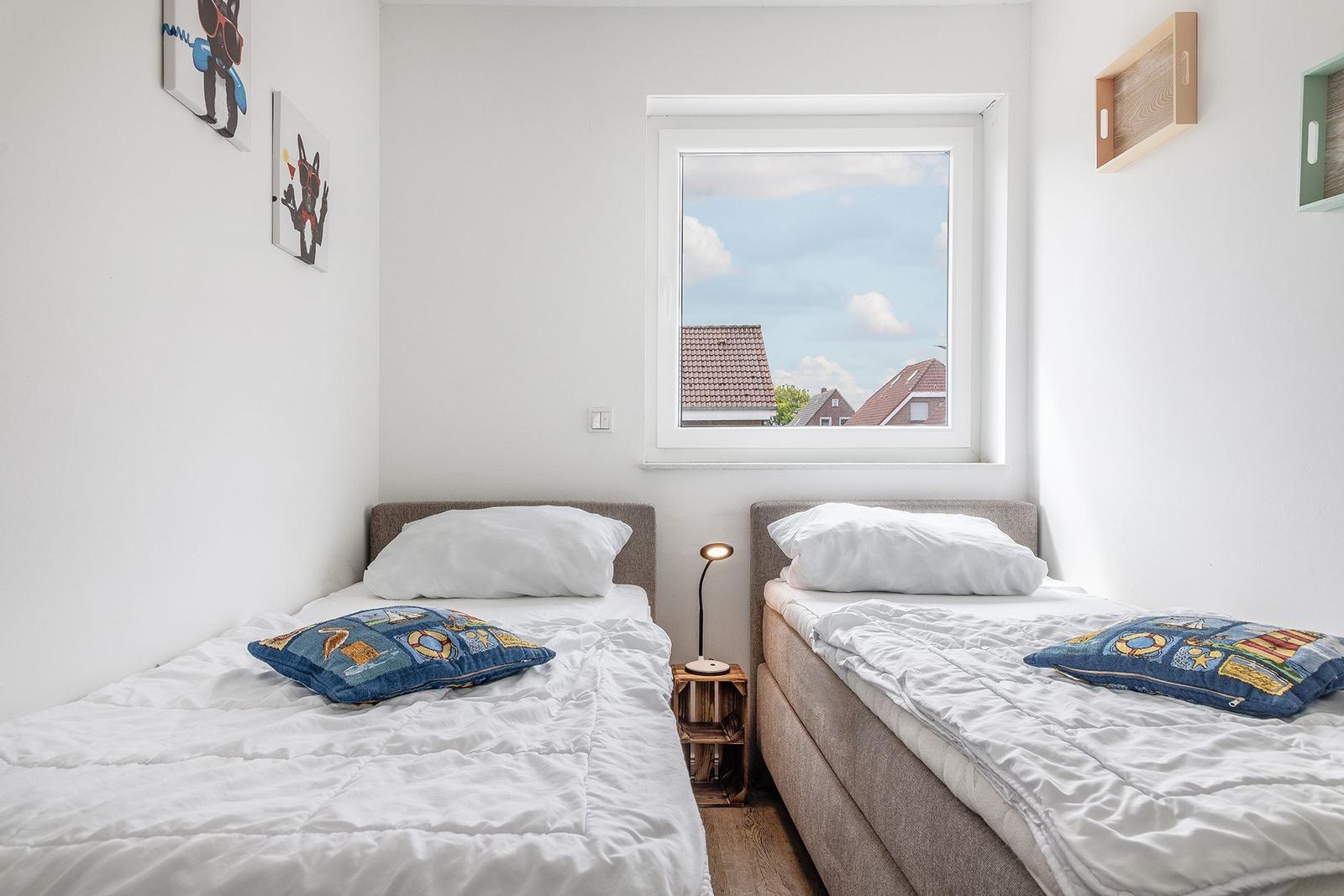Zwei Einzelbetten mit weißen Bettwäsche und blauen Kissen. Fenster mit Blick auf Dächer.