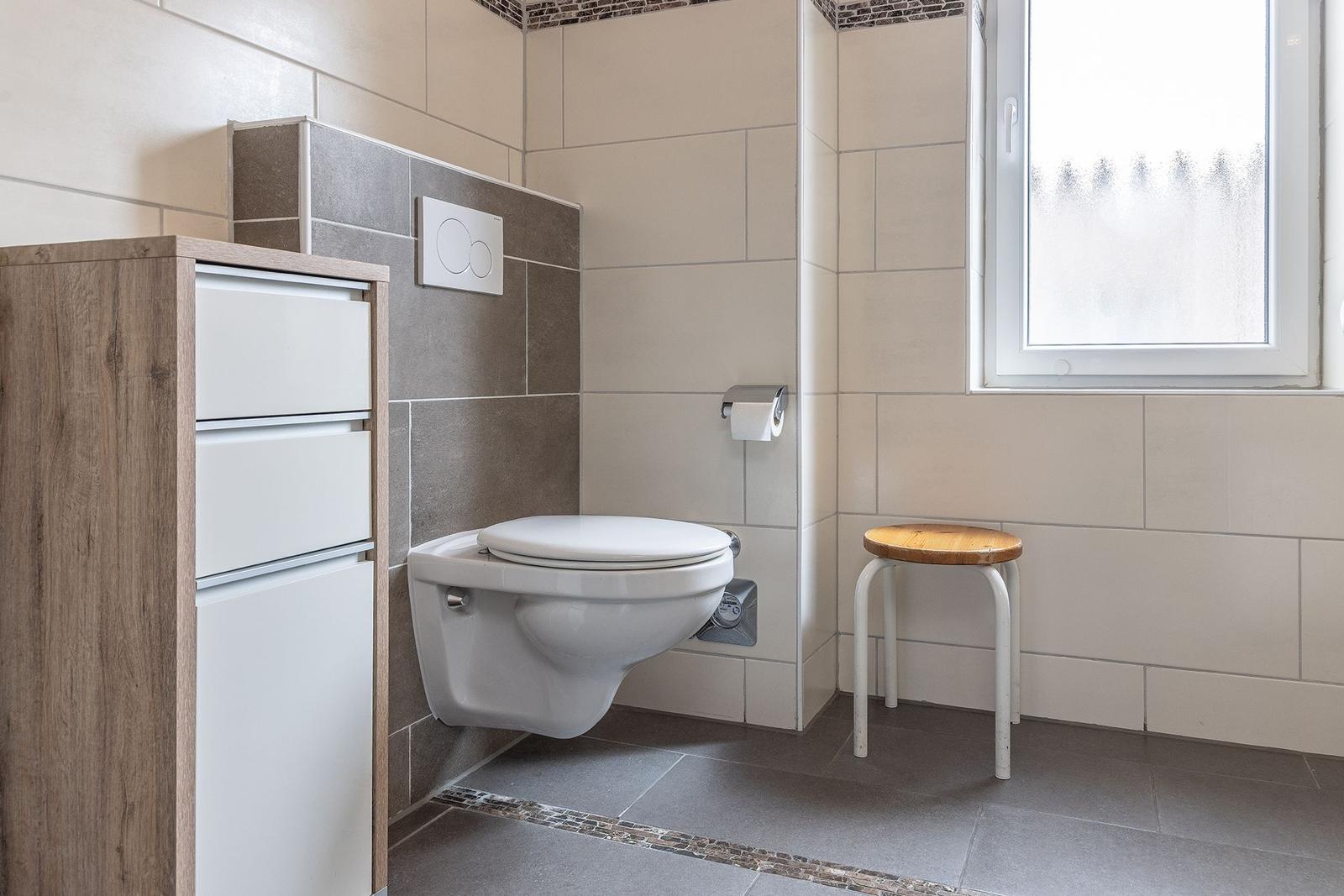 Badezimmer mit Toilette, Holzstuhl und Fenster.