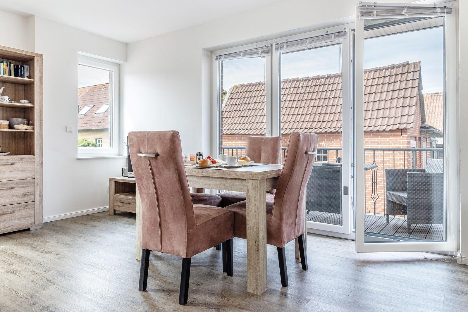 Essbereich mit Tisch, Stühlen und Blick auf Balkon mit Gartenmöbeln.