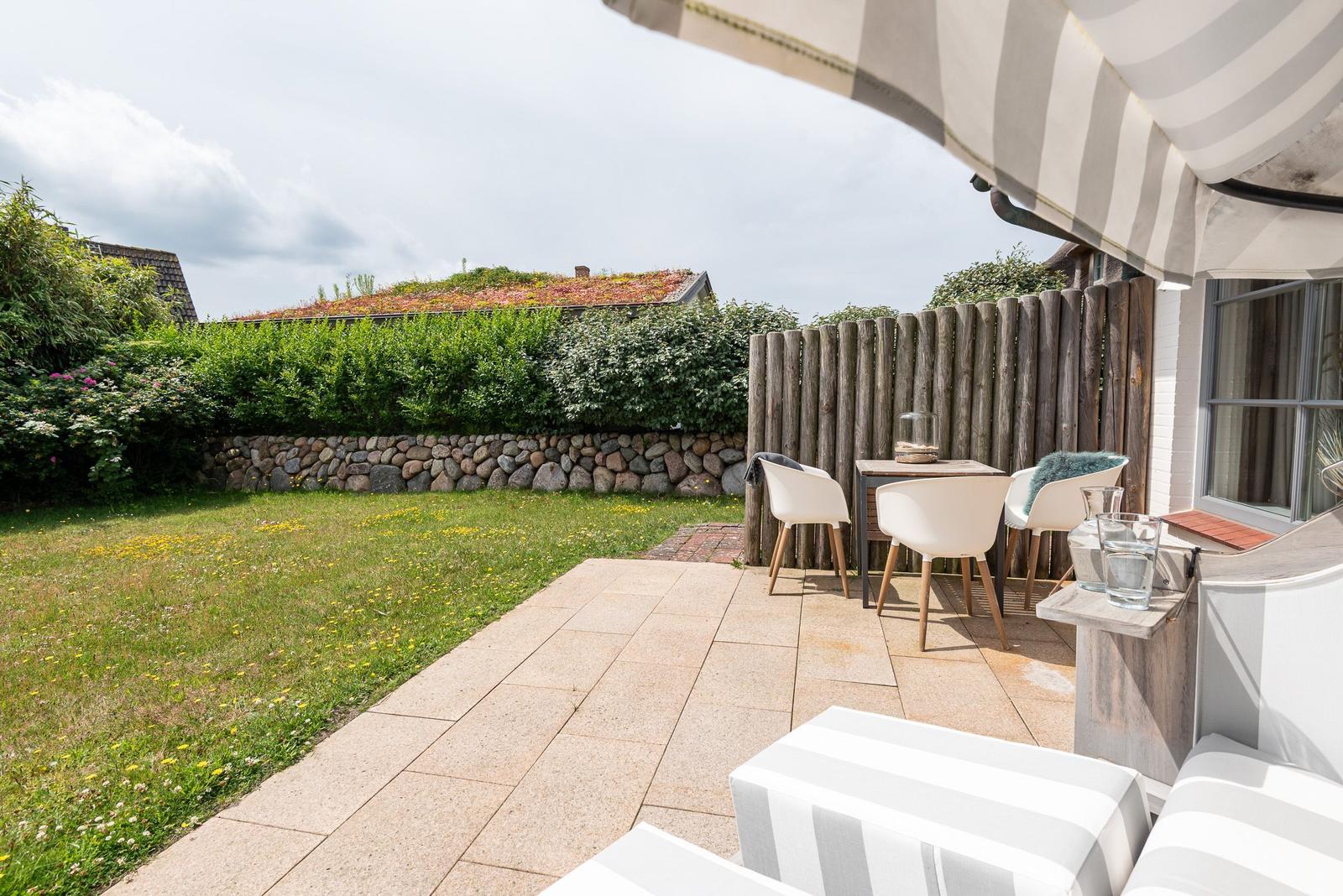Terrace with seating, awning, and view of green garden with stone wall.