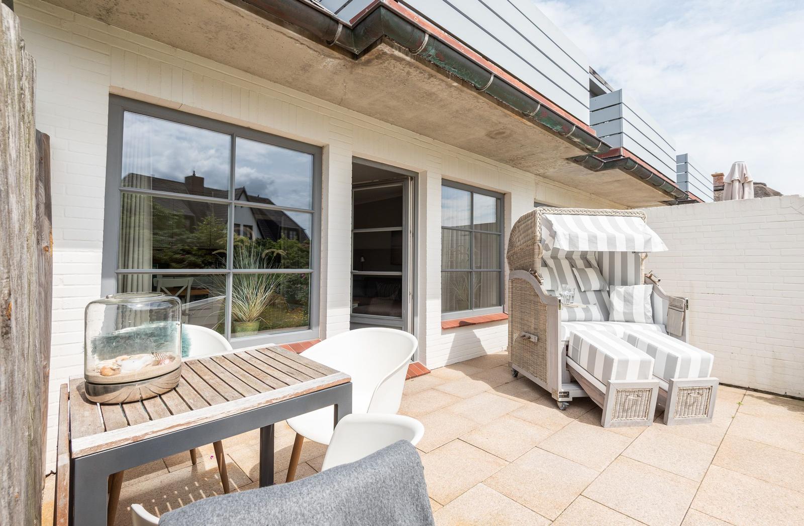 Terrace with lounge furniture, table and chairs. White wall and large windows.