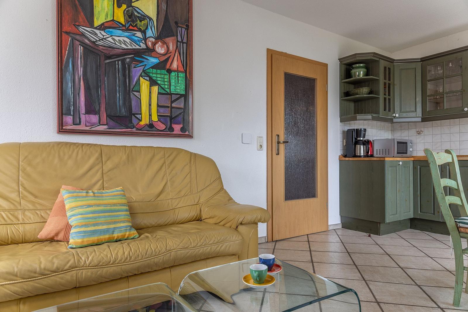Ein Wohnzimmer mit Sofa, Glas-Tisch und Küchenbereich mit grünen Schränken.