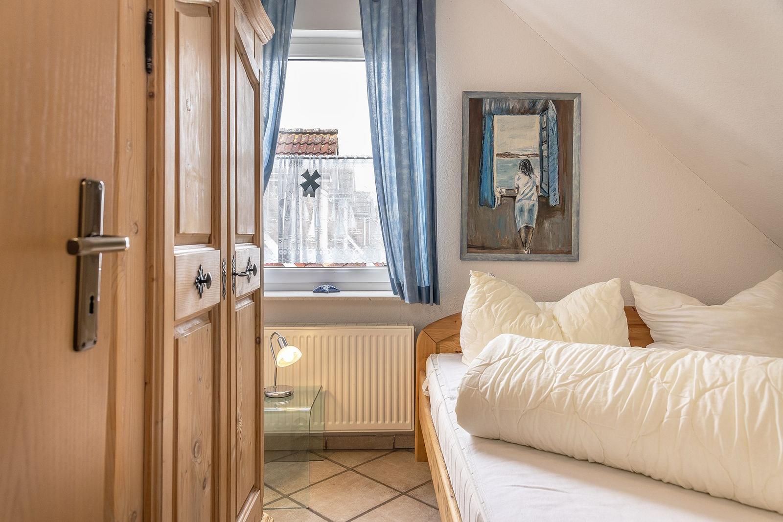 Schlafzimmer mit Bett, Fenster, Gardinen und Bild an der Wand.