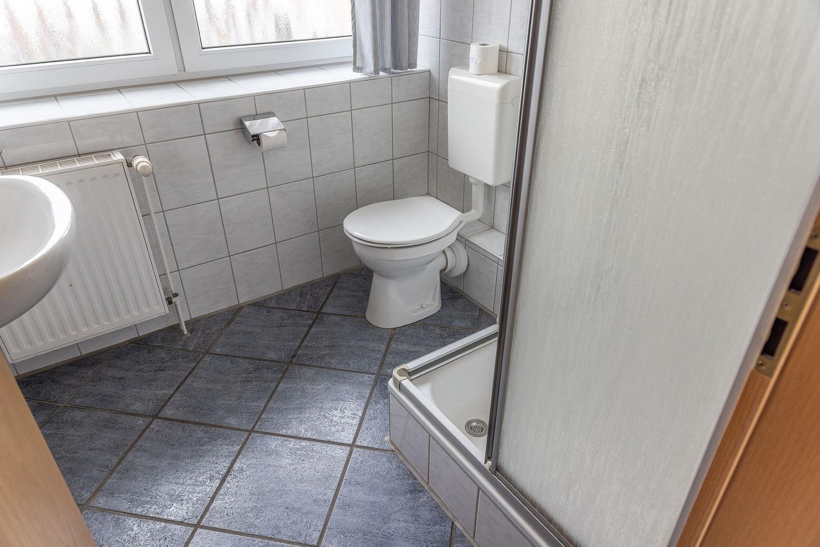 Badezimmer mit Toilette, Dusche und Waschbecken. Fliesenboden und Fenster.