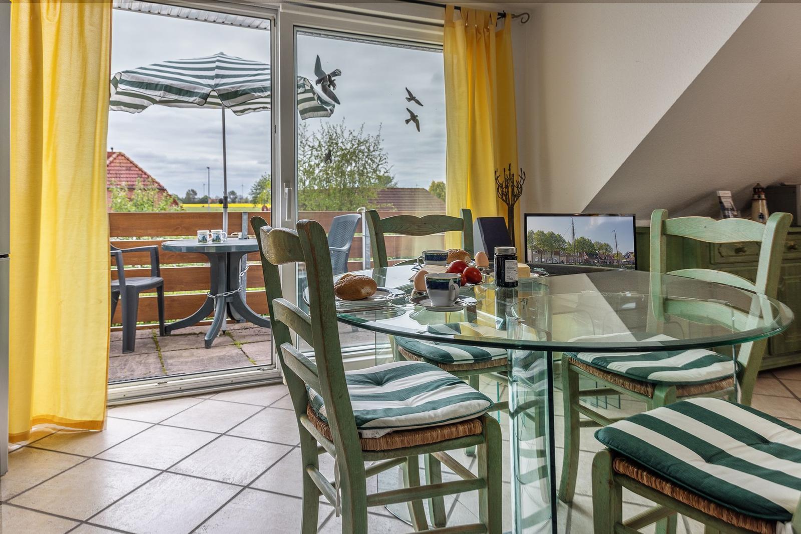 Glasrundtisch mit Stühlen, Blick auf Balkon mit Sonnenschirm.