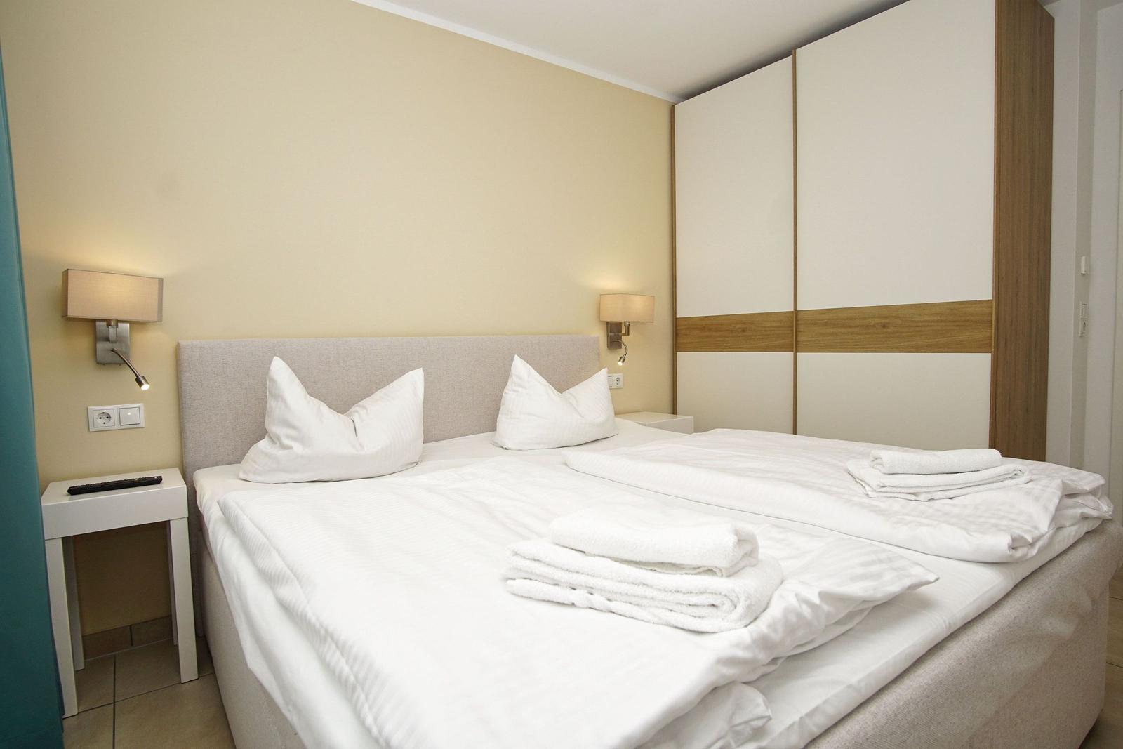 Schlafzimmer mit Doppelbett, weißen Bettwäsche und Nachttischen mit Lampen.