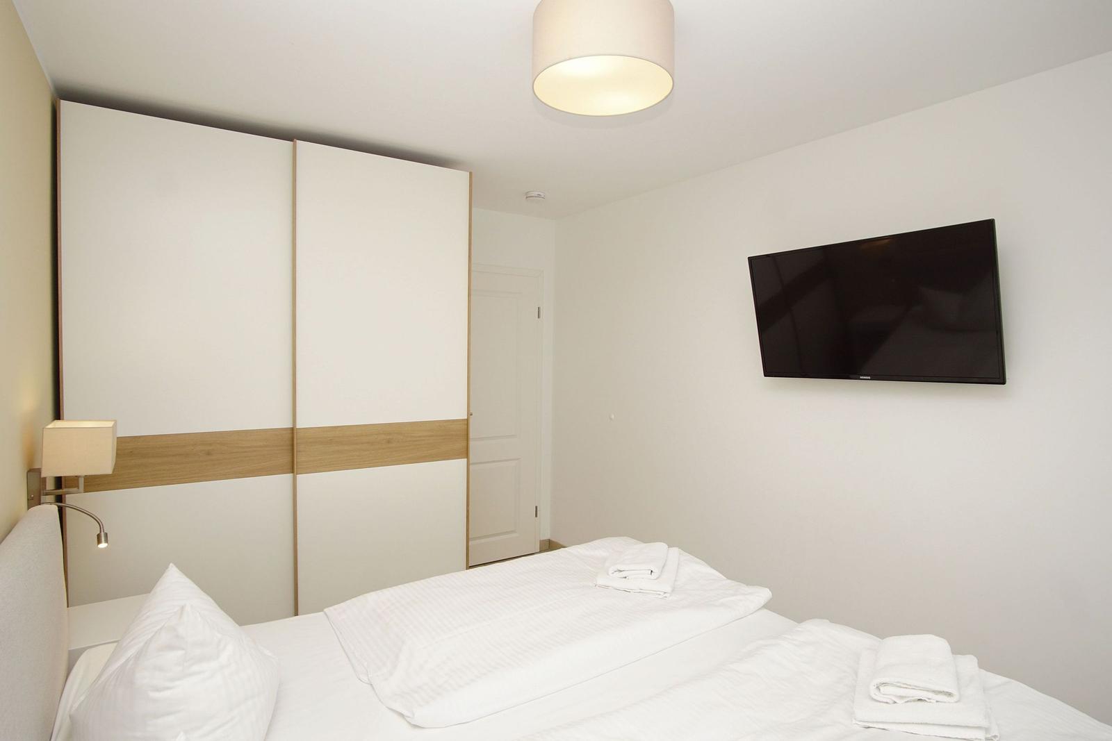 Schlafzimmer mit Bett, Kleiderschrank und Wandfernseher.