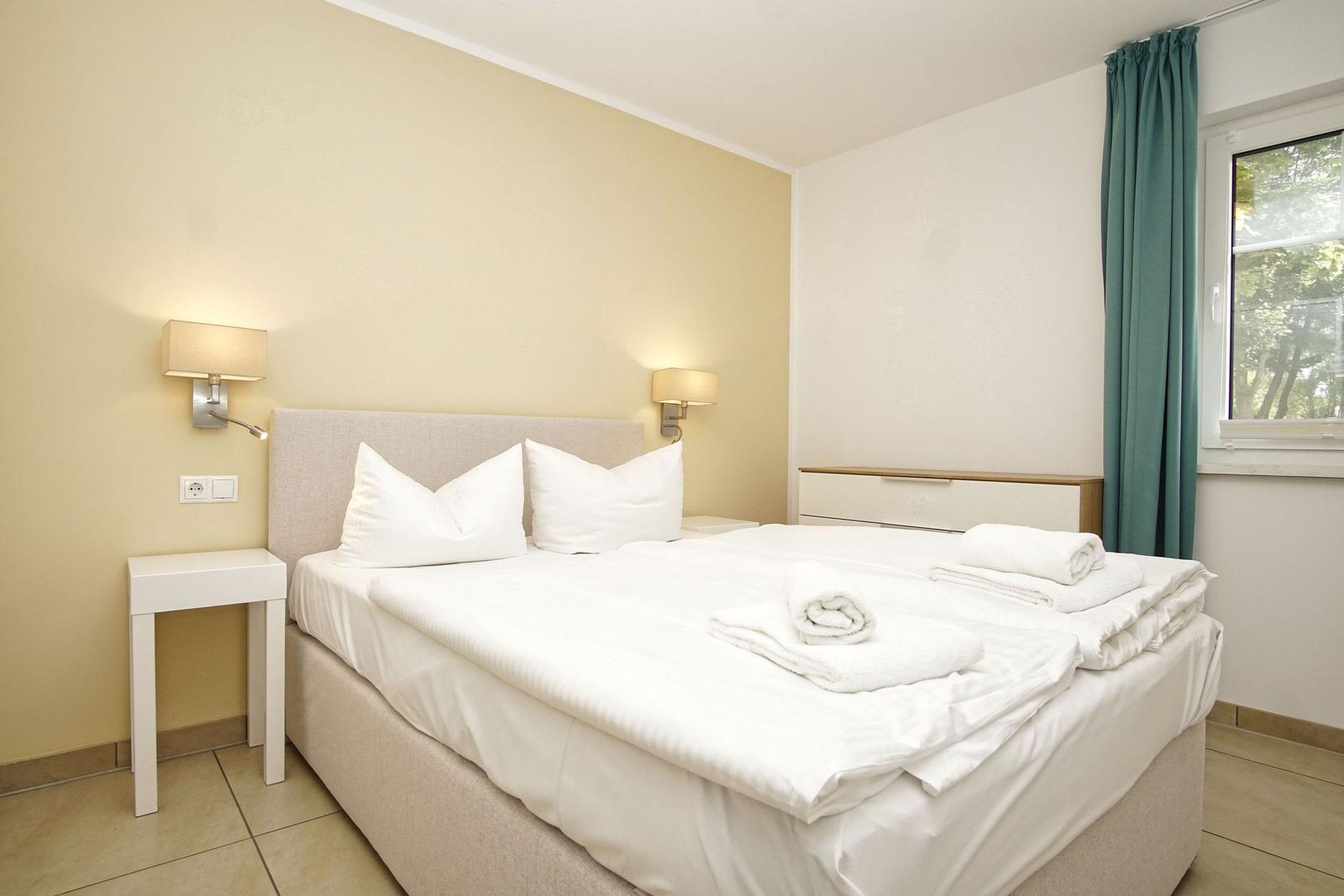 Schlafzimmer mit Bett, Nachttisch und Fenster mit Vorhängen.
