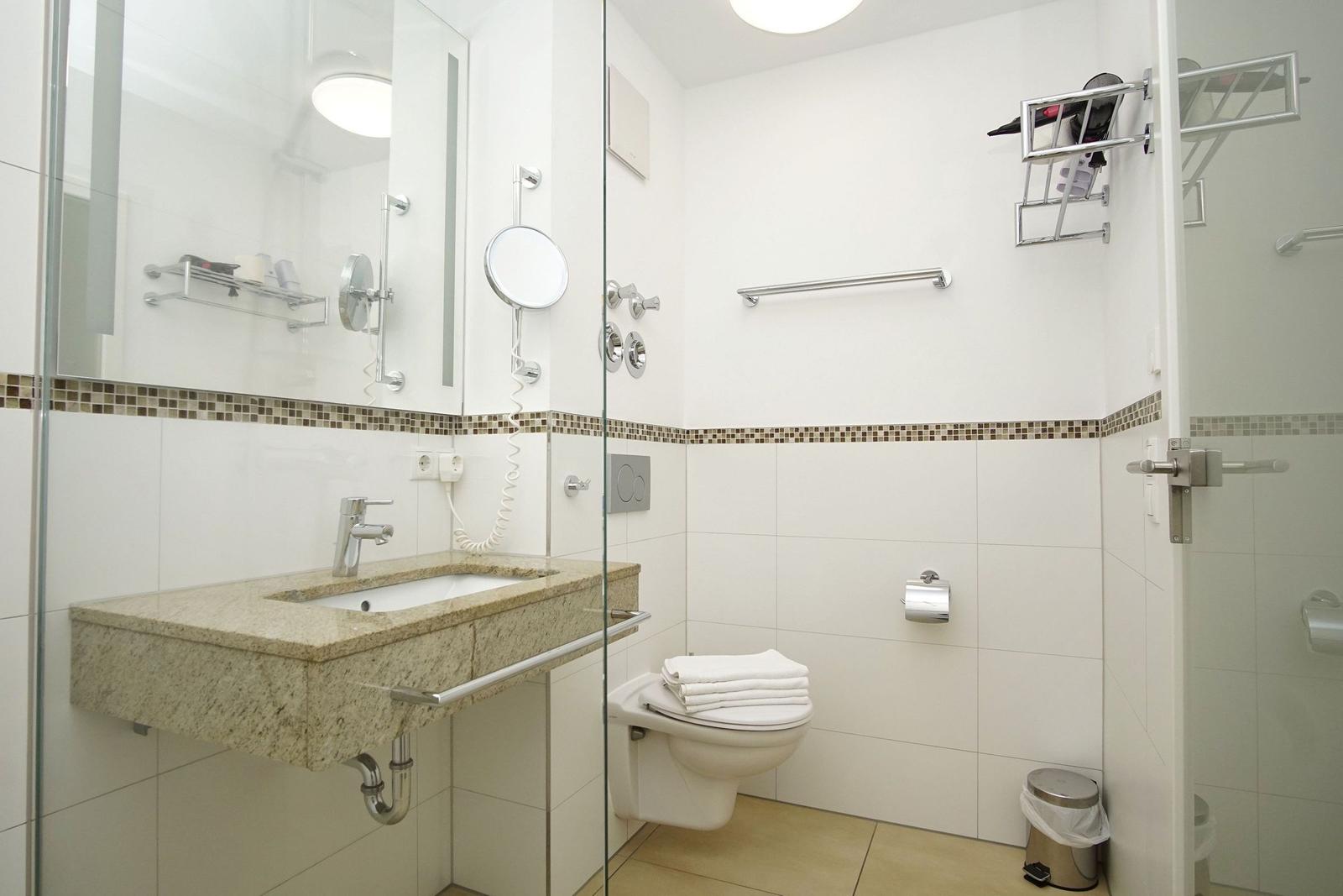 Badezimmer mit Waschbecken, Toilette und Dusche. Weiße Fliesen und Mosaikband.