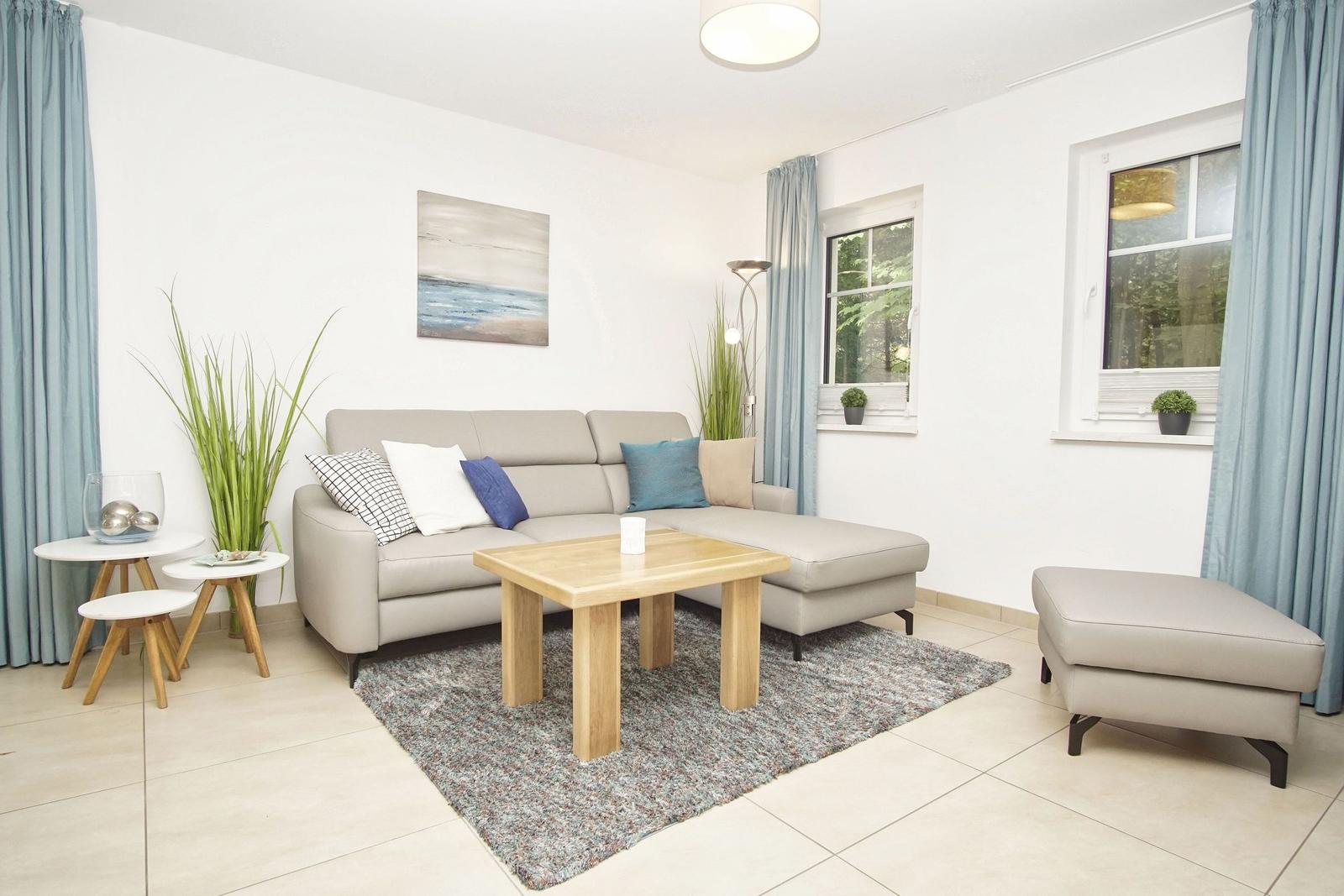 Ein Wohnzimmer mit grauem Sofa, Holztisch und blauen Vorhängen.