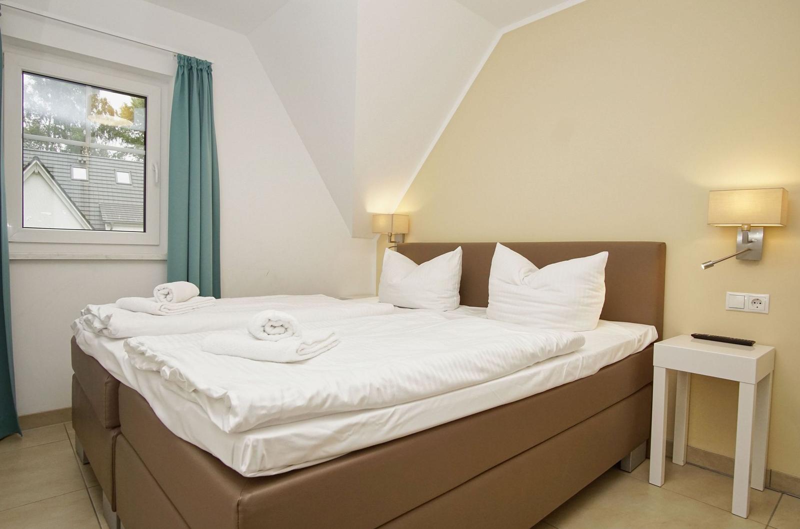Schlafzimmer mit Doppelbett, Fenster und Nachttisch.