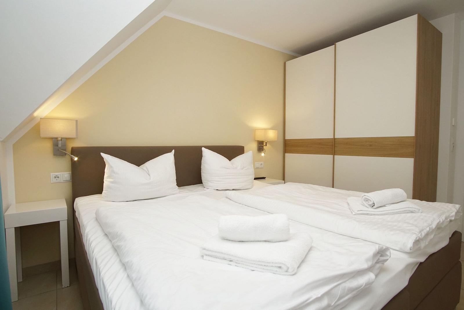 Schlafzimmer mit Doppelbett, Nachttischen und Kleiderschrank unter Dachschrägen.