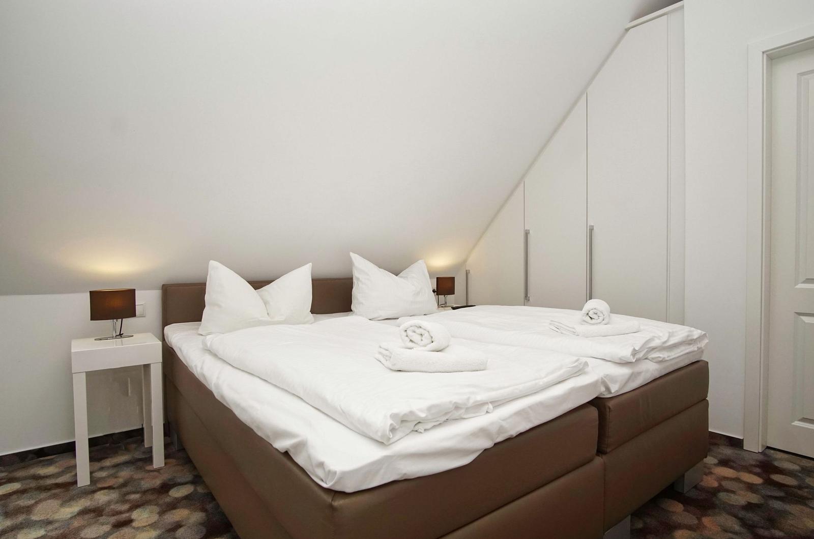 Doppelbett mit weißer Bettwäsche, Nachttische und Kleiderschrank unter Dachschräge.
