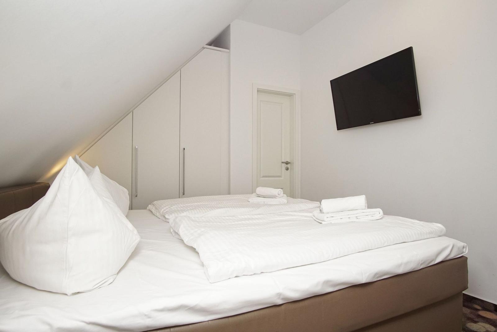 Schlafzimmer mit Bett, Kleiderschrank und Wandfernseher.