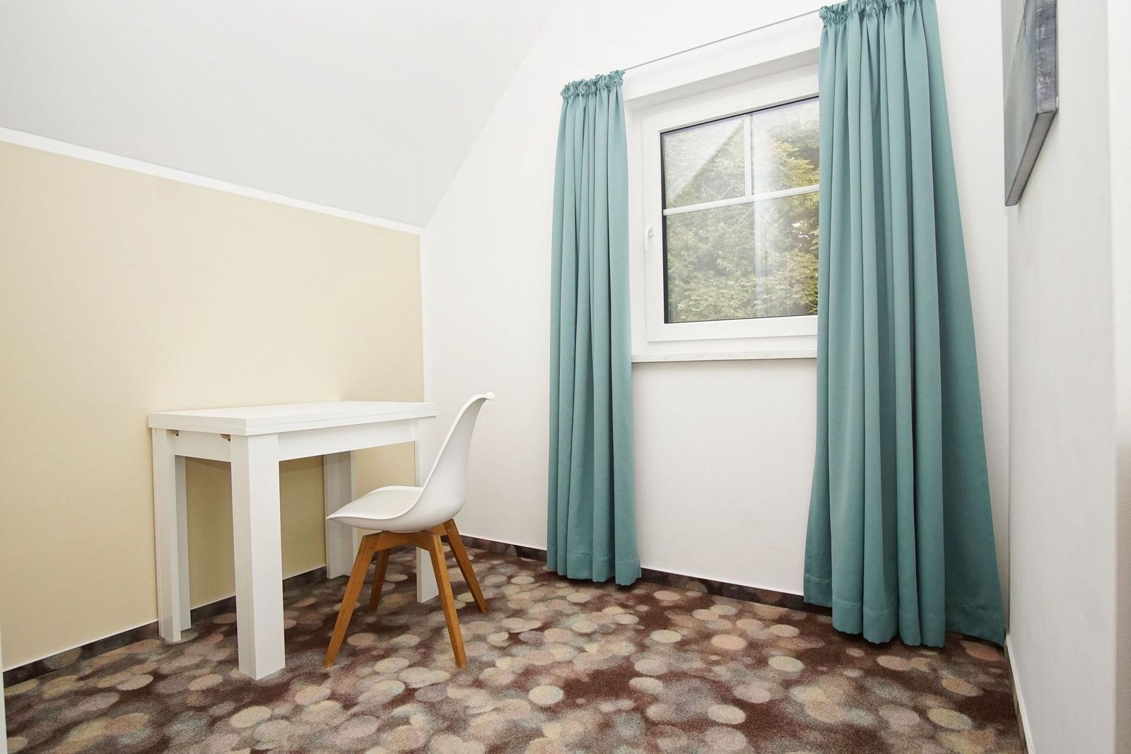 Ein Zimmer mit Schreibtisch, Stuhl und Fenster mit Vorhängen.