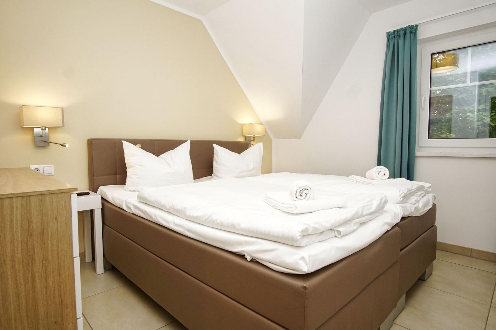 Schlafzimmer mit Doppelbett, weißen Bettwäsche und Fenster mit grünen Vorhängen.