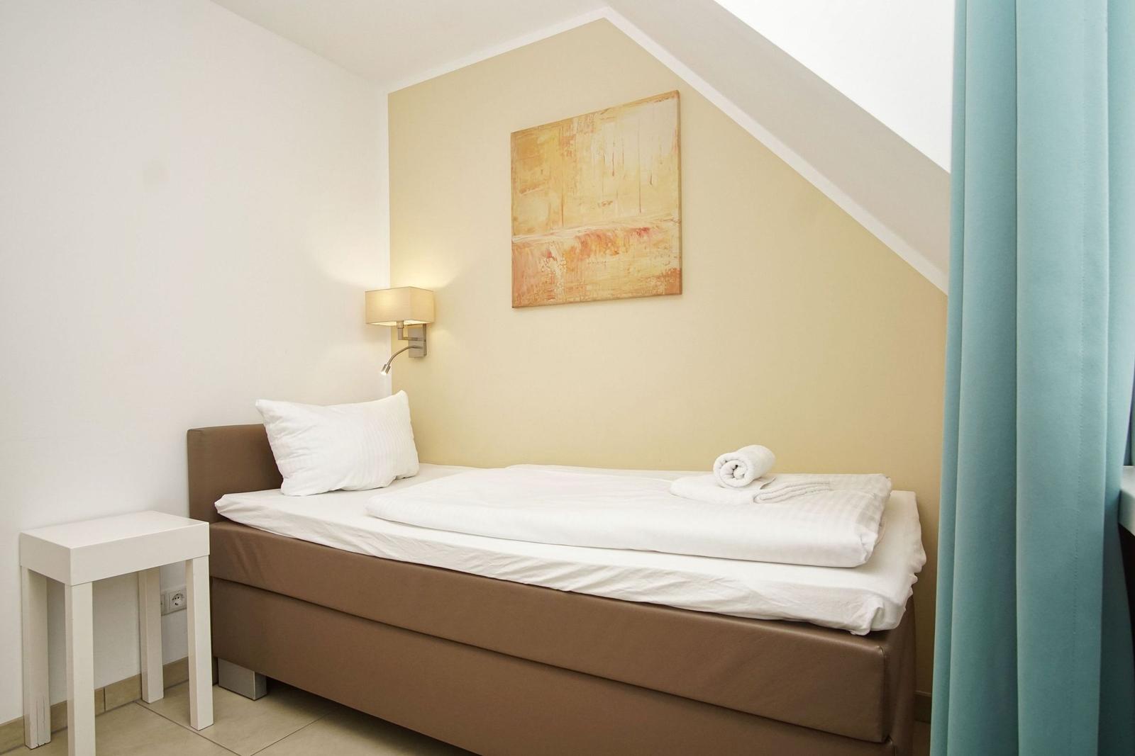 A bedroom with bed, nightstand, and wall lighting. A picture hangs on the wall.
