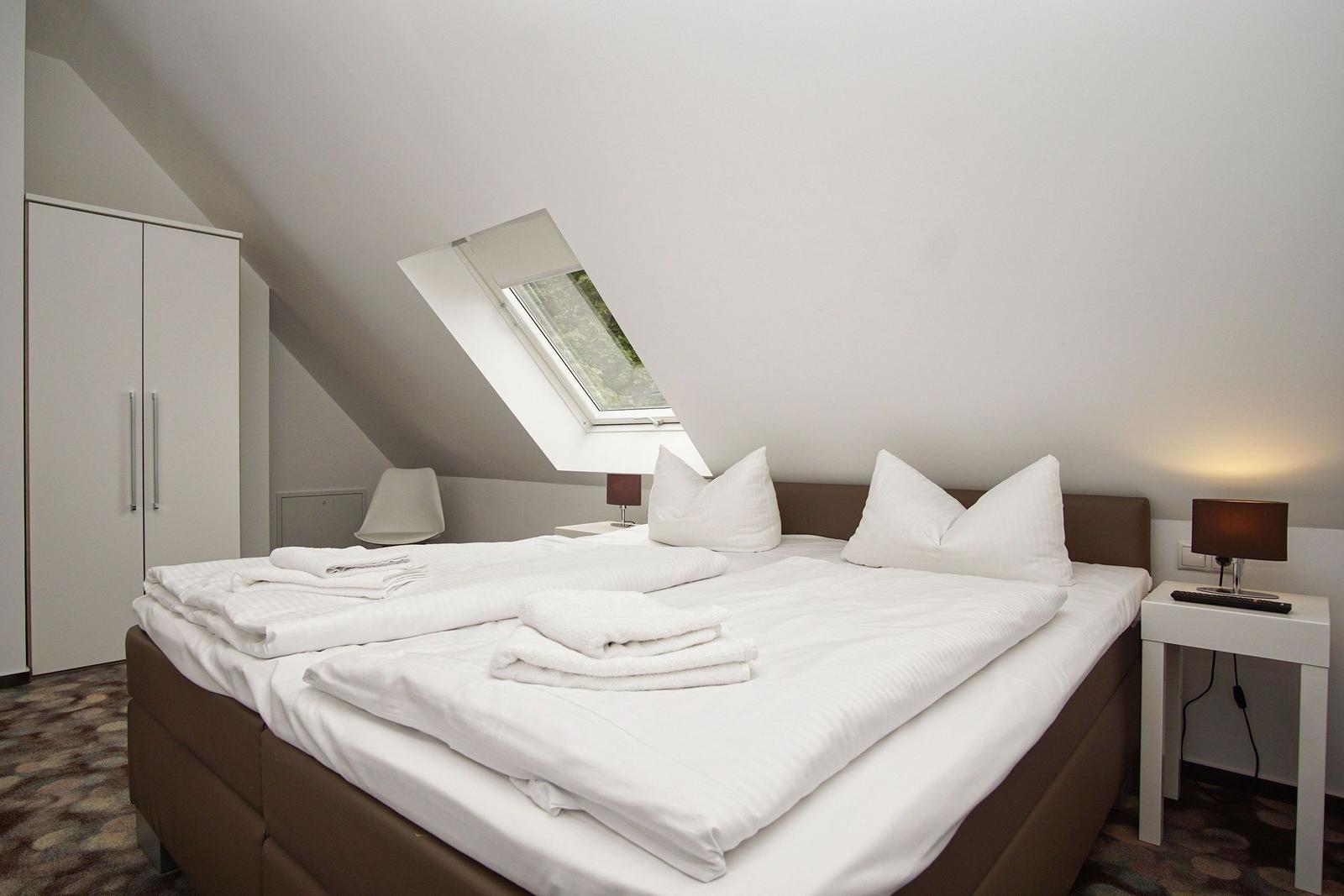 Bedroom with sloped ceiling, skylight, and bed with white bedding.