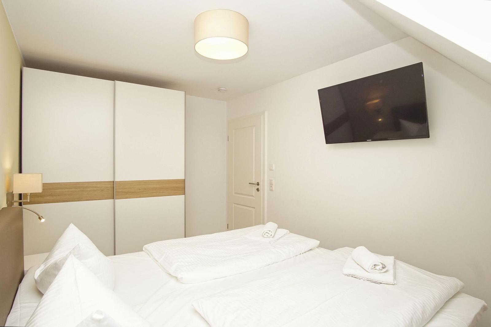 Schlafzimmer mit Doppelbett, Schrank und Wandfernseher.