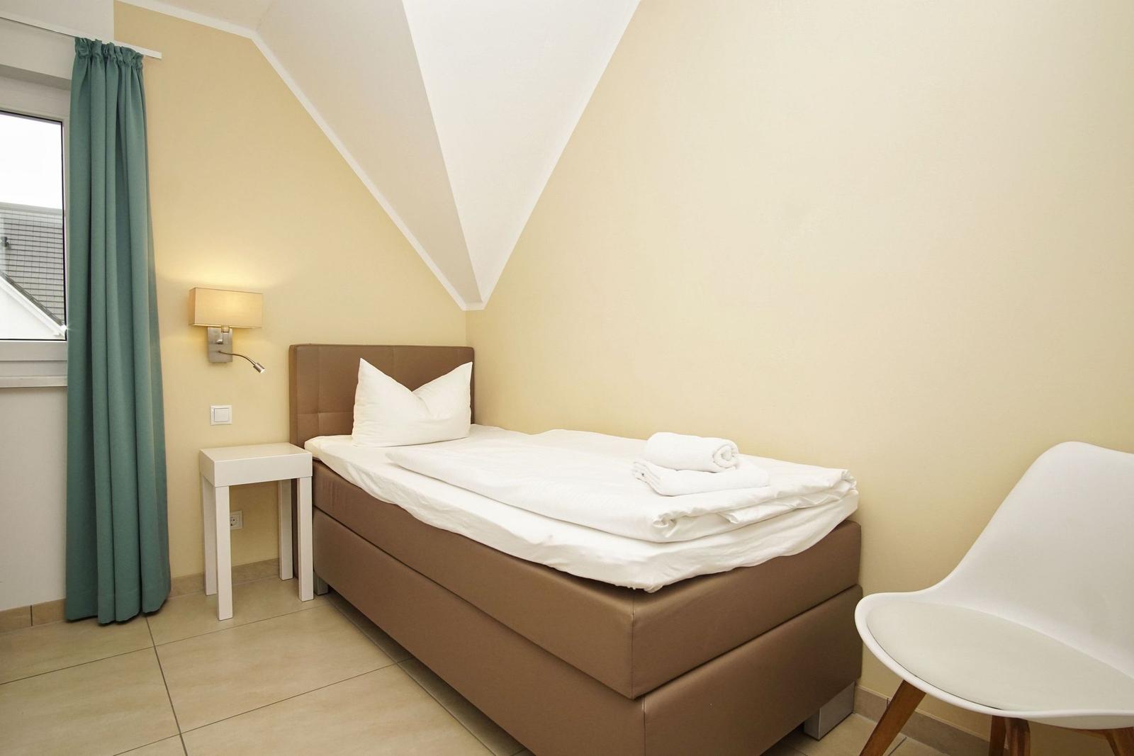 Ein Schlafzimmer mit einem Bett, einem Stuhl und einem Nachttisch neben dem Fenster.