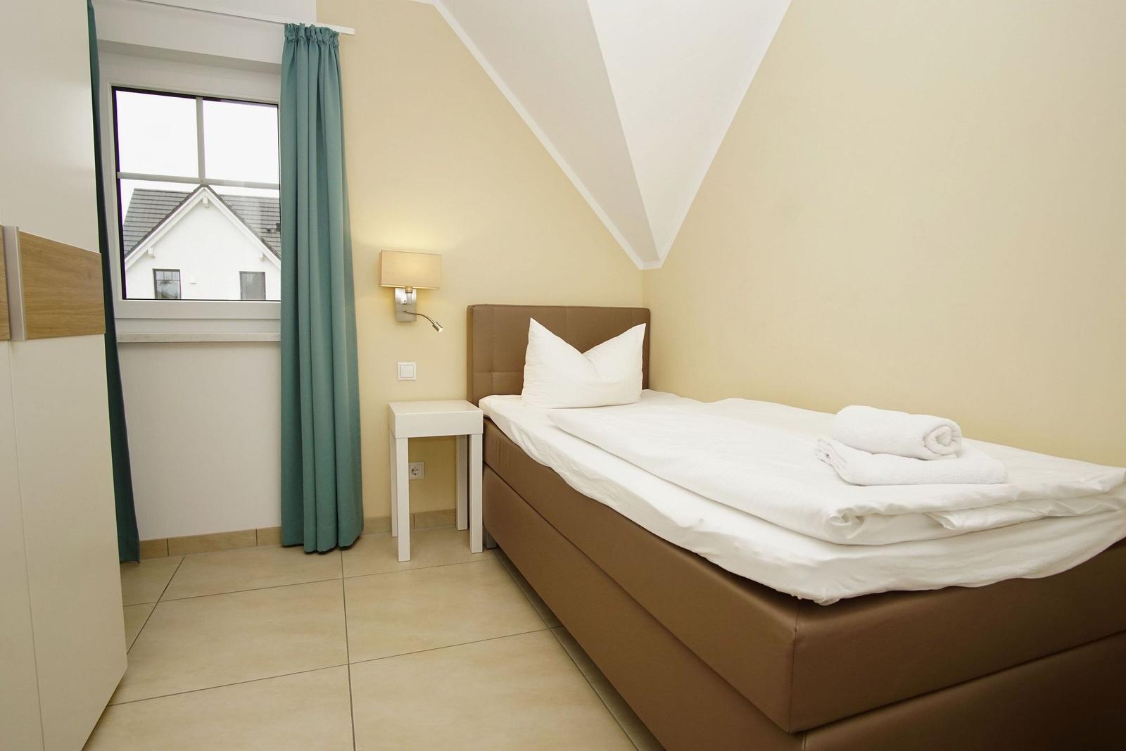Ein Schlafzimmer mit Bett, Nachttisch und Fenster mit Vorhang.