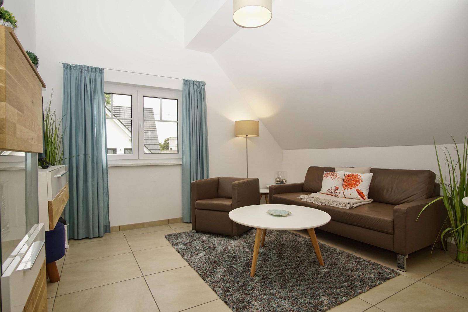 Wohnzimmer mit braunem Sofa, runden Tisch und blauen Vorhängen an Fenster.
