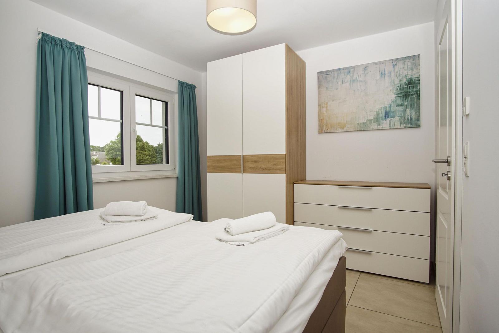 Schlafzimmer mit Bett, Schrank und Fenster mit Vorhängen.