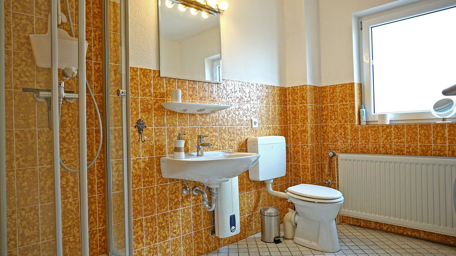 Badezimmer mit Dusche, Waschbecken und Toilette. Wände mit gelben Fliesen.