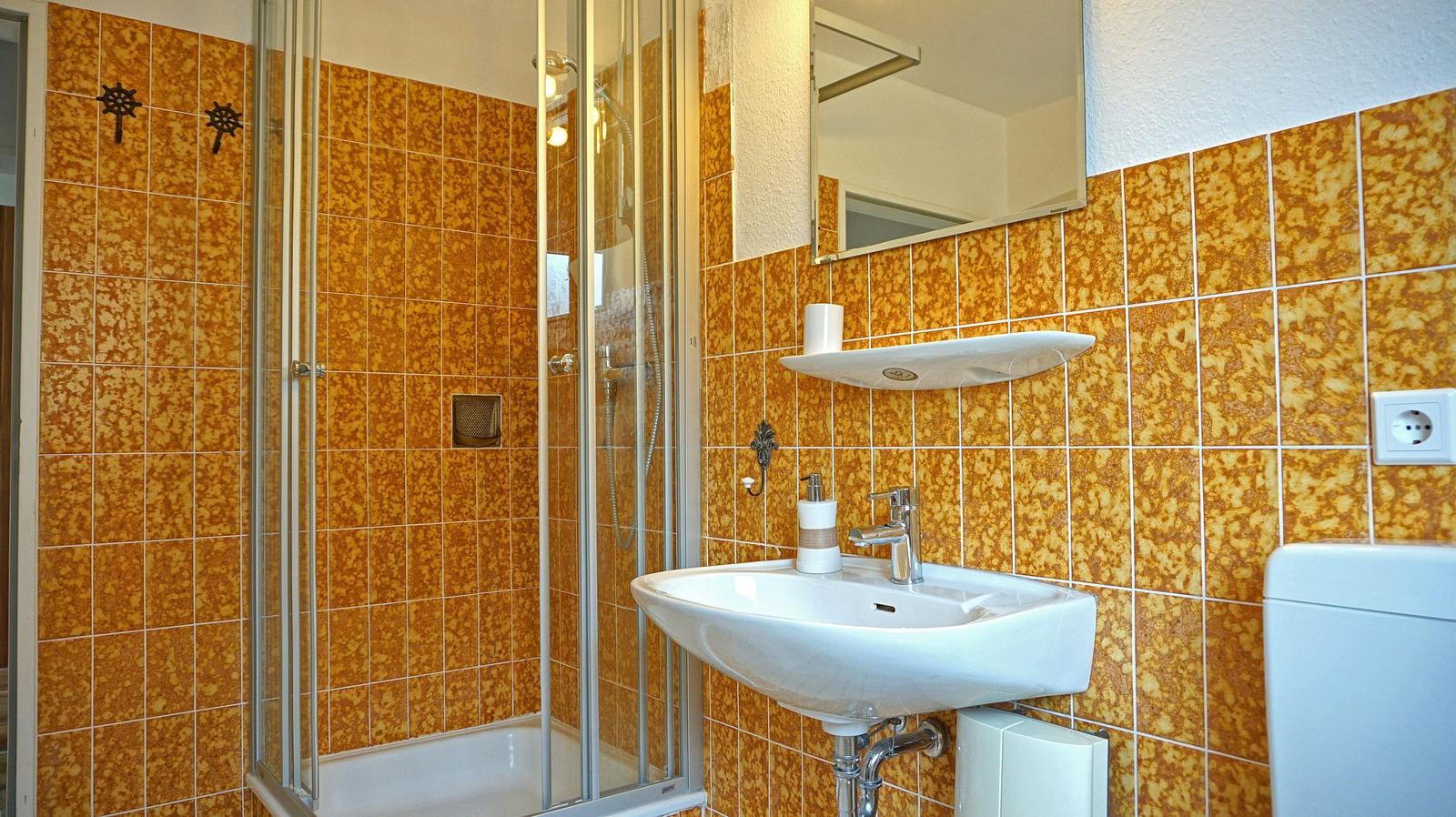 Bad mit Dusche, Waschbecken und Toilette. Wände mit orangefarbenen Fliesen.