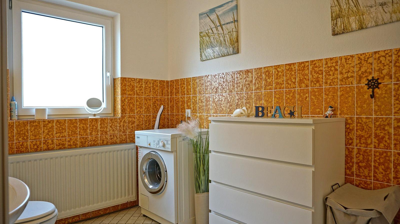 Wohnraum mit Waschmaschine, Schrank und Fenster. Wand mit orangefarbenen Fliesen.