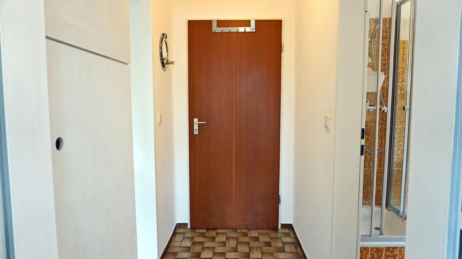 Flur mit Holztür, Fliesenboden und Blick in die Dusche.