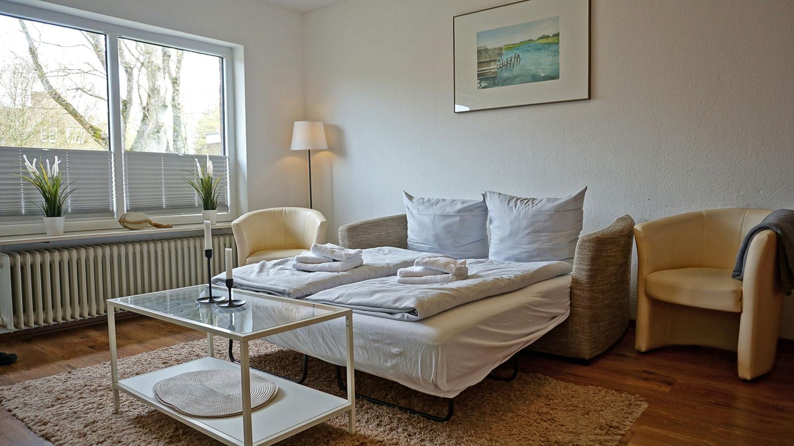 Ein Schlafzimmer mit Bett, zwei Sesseln und einem Tisch vor einem Fenster.