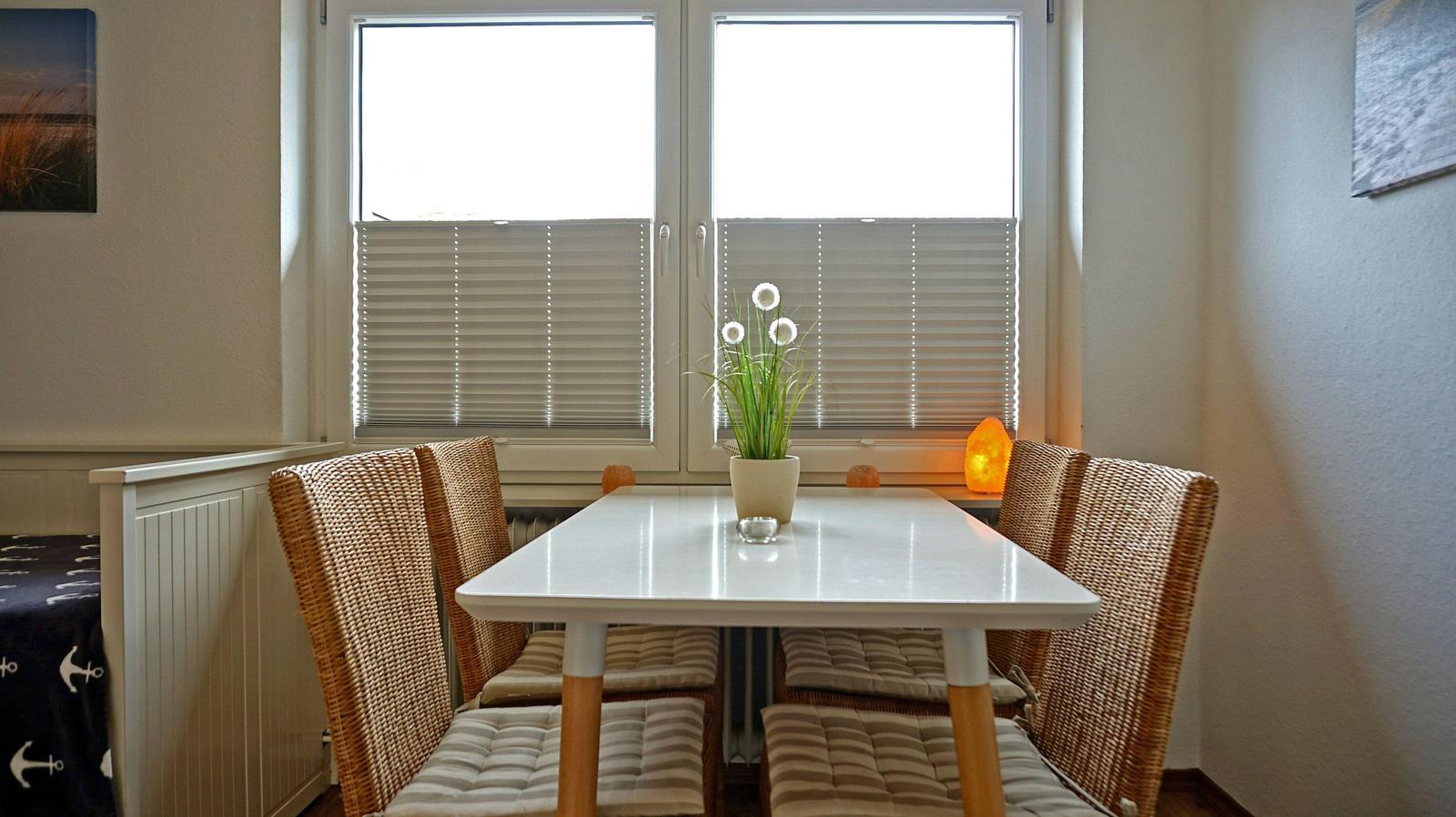 Essbereich mit Tisch, vier Stühlen und Fenster mit Jalousien.