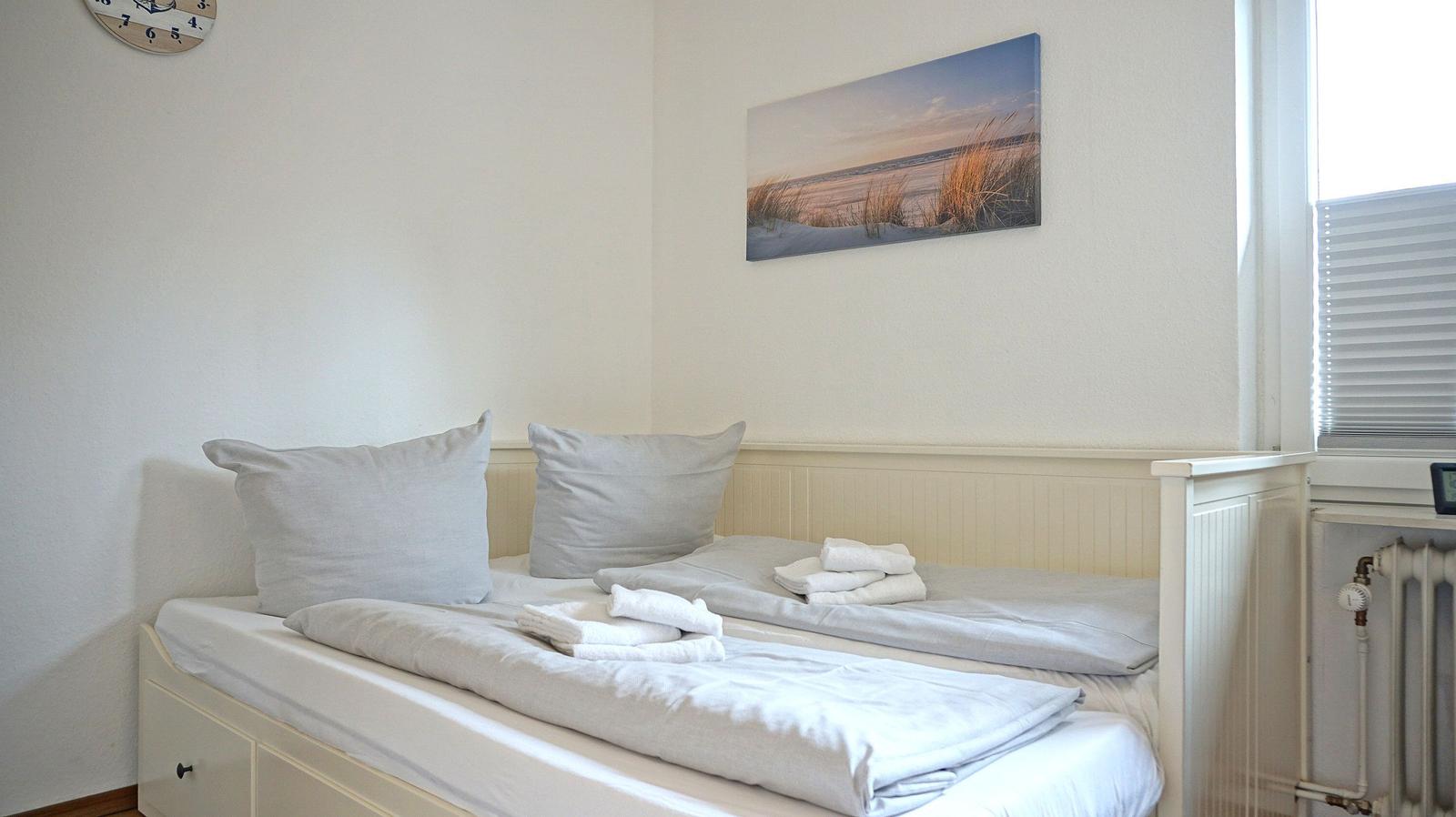 Schlafzimmer mit Doppelbett, Wandbild und Fenster mit Jalousie.
