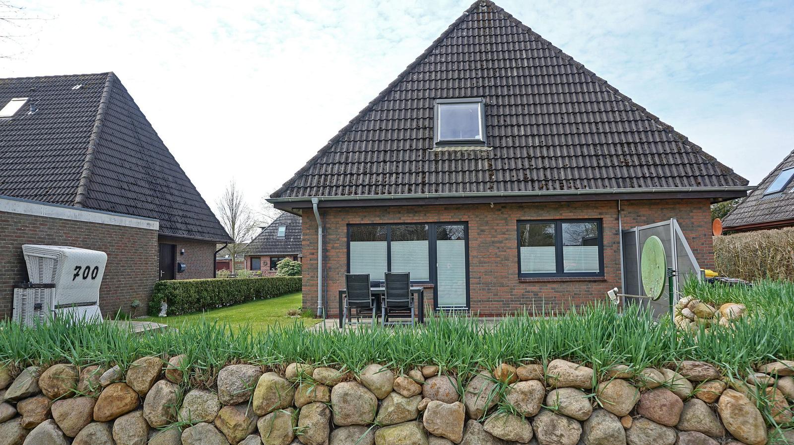 Einfamilienhaus mit Terrasse und Garten. Steinmauer im Vordergrund.